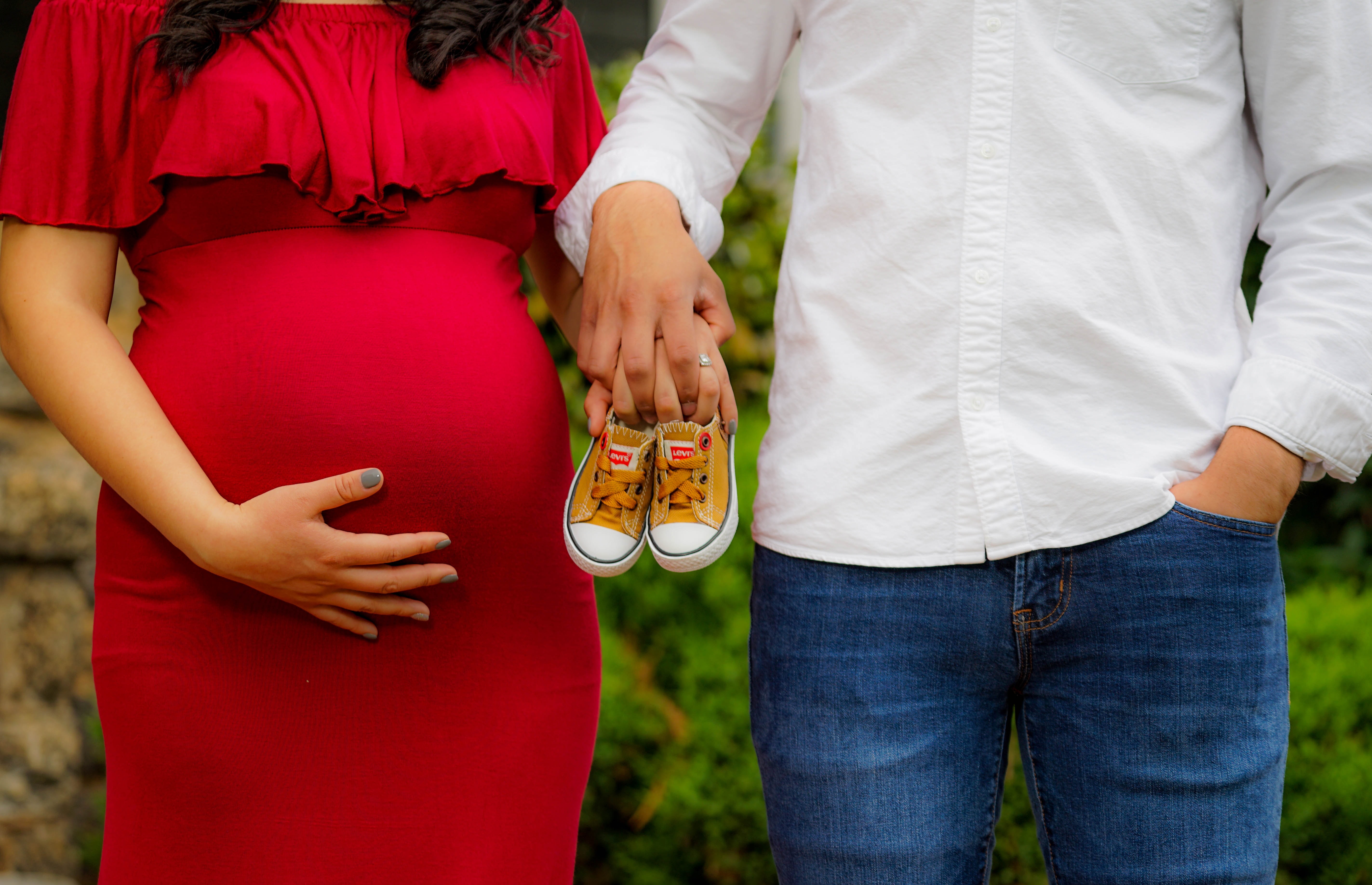 pregnant mom holding hands with husband and holding baby shoes