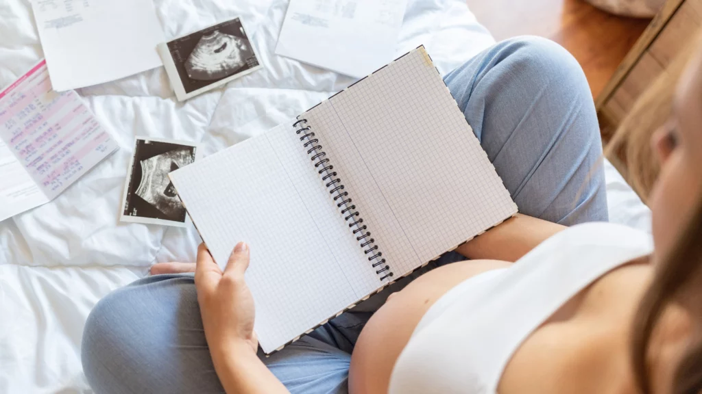 Woman writing in pregnancy journal with sonograms in front of her