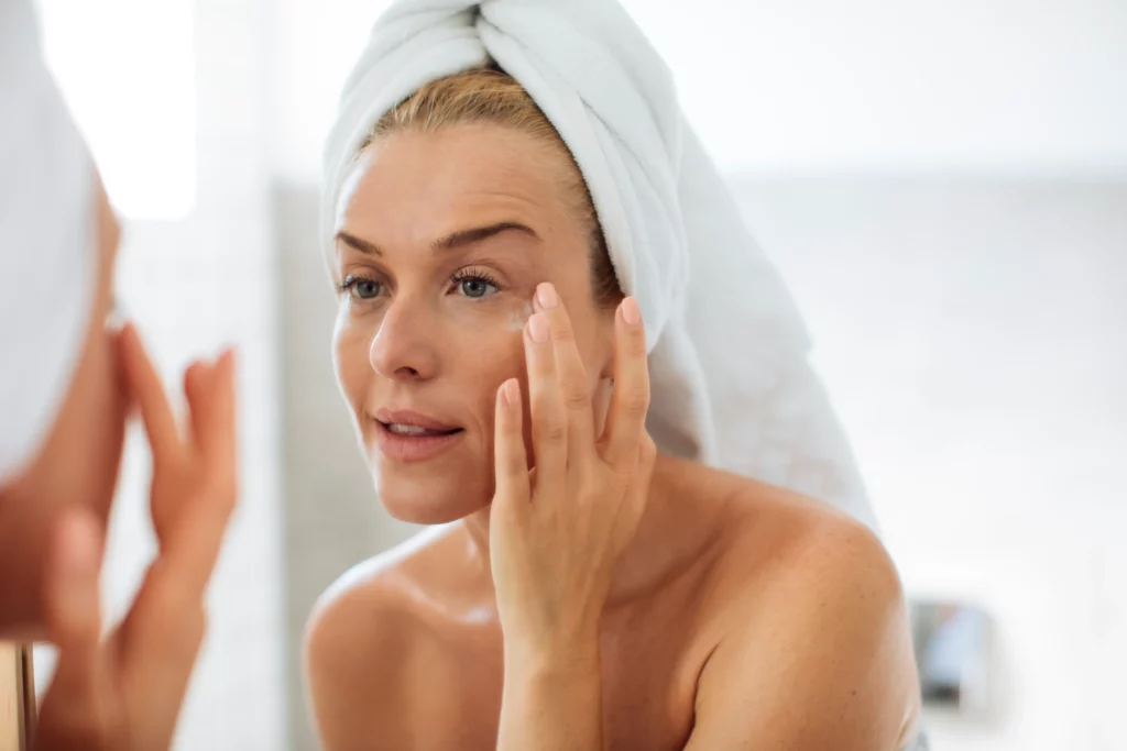 Woman engaging in a self-care night with skincare and adding lotion on her face with hair wrapped in towel